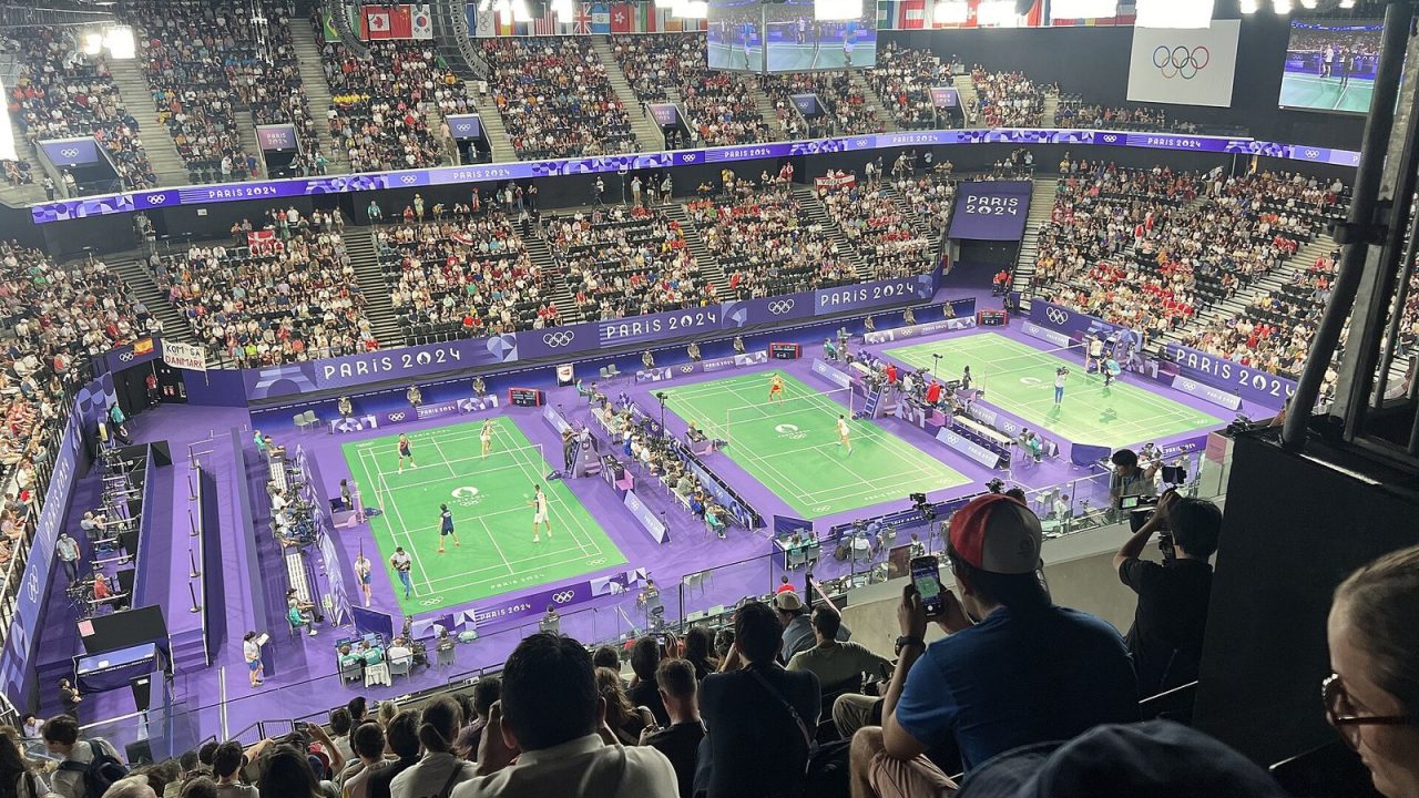 Three badminton courts in use under the lights at the Porte de la Chapelle Arena during the Paris 2024 Olympics
