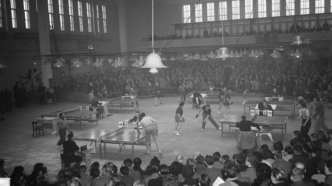 Black-and-white view of a packed hall with several table tennis tables in play at an international event in Utrecht