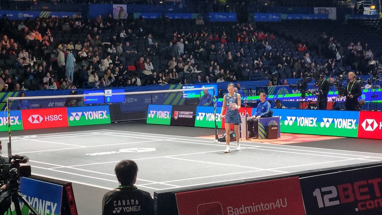 A player on court at the 2026 All England Open in Birmingham, with crowd and sponsor boards behind