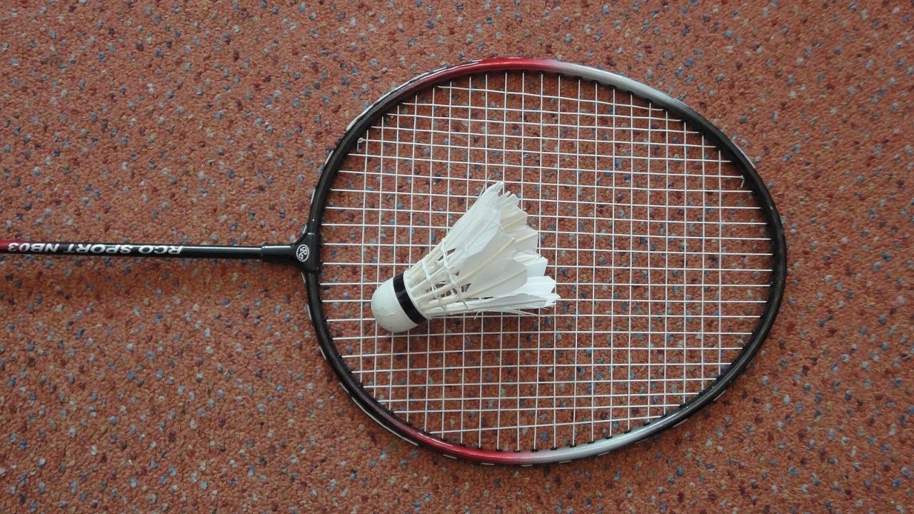 Badminton racket lying with a feather shuttlecock on a wooden floor