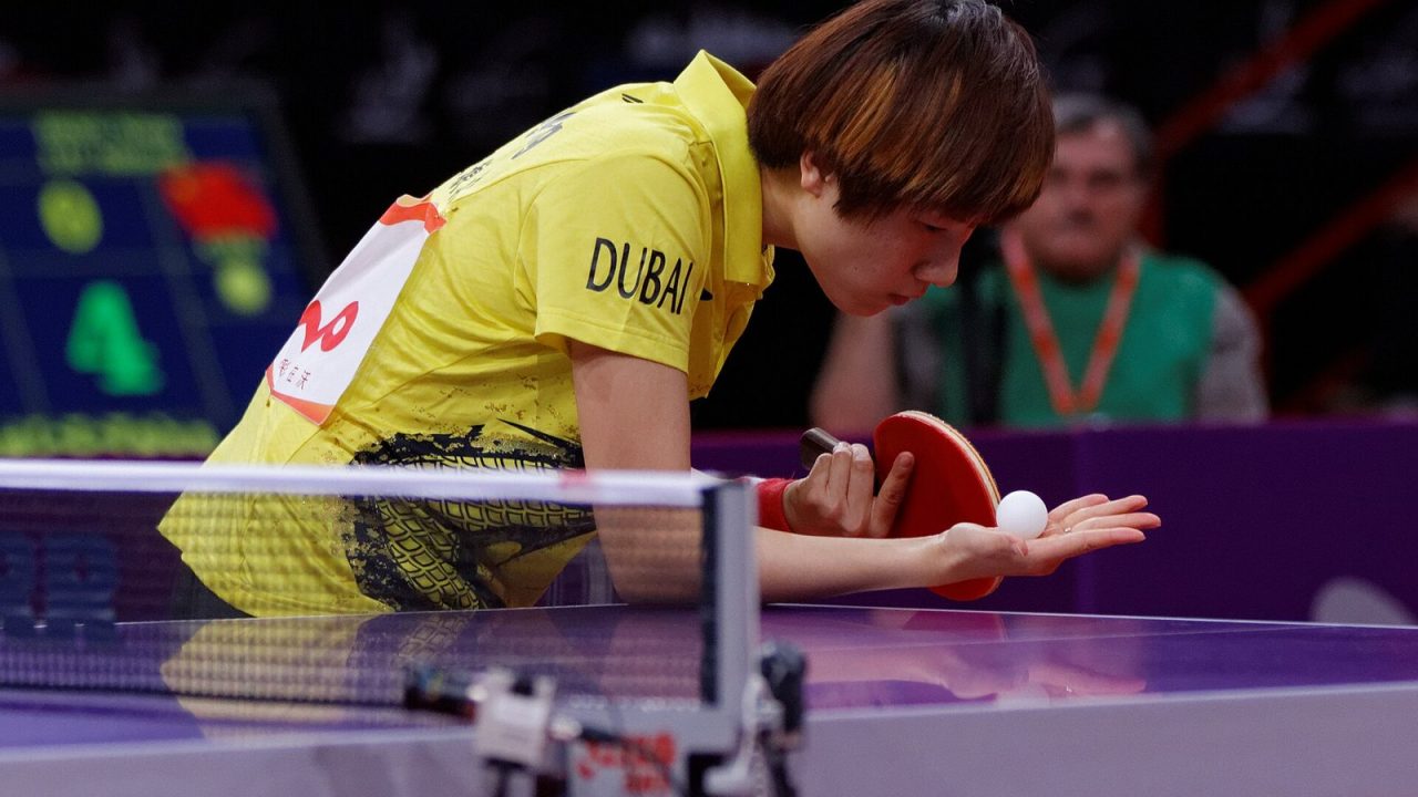 Player resting the ball on a flat open palm behind the table before serving in a doubles final