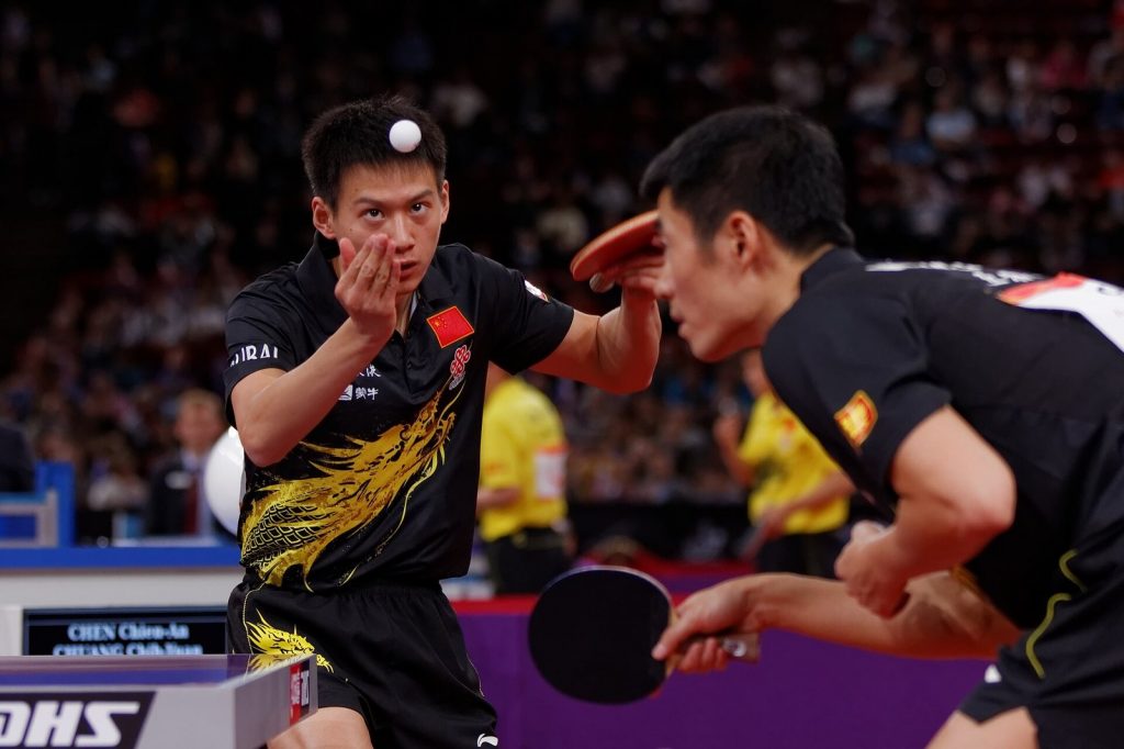 Player tossing the ball to serve while his doubles partner stands beside him