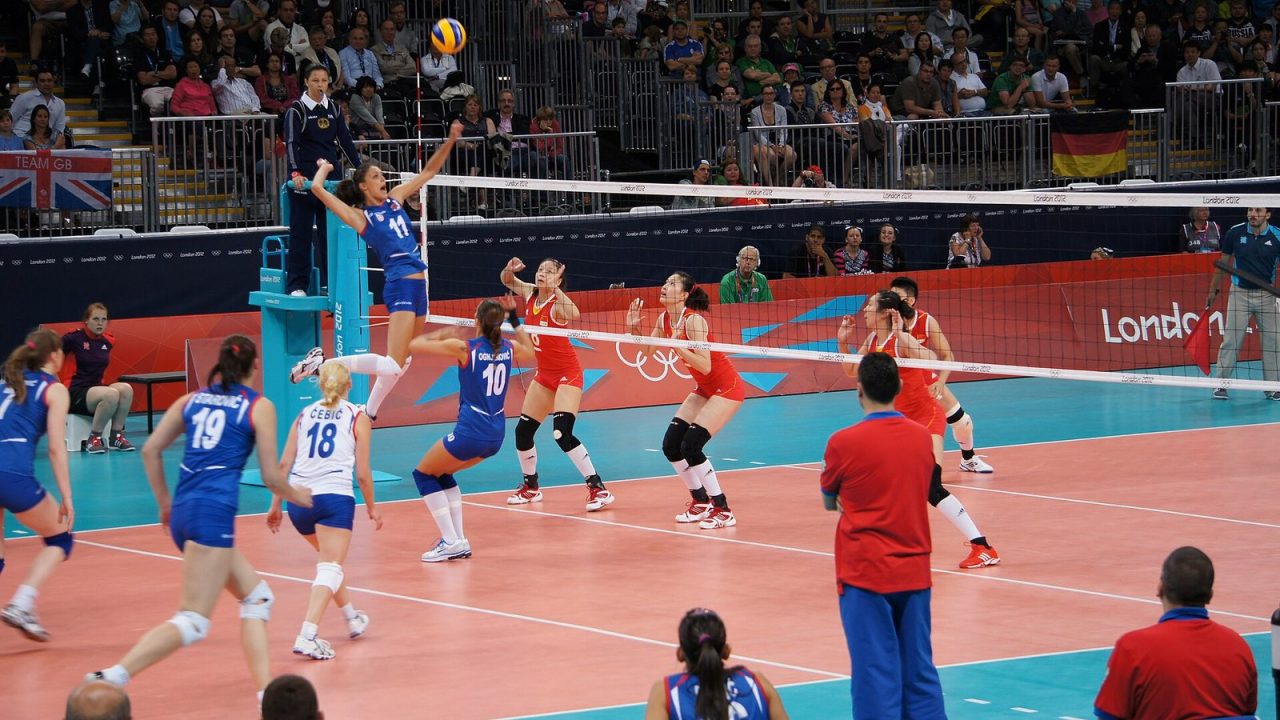 A player jumping at the net as the ball rises during a women's indoor match at the London 2012 Olympics